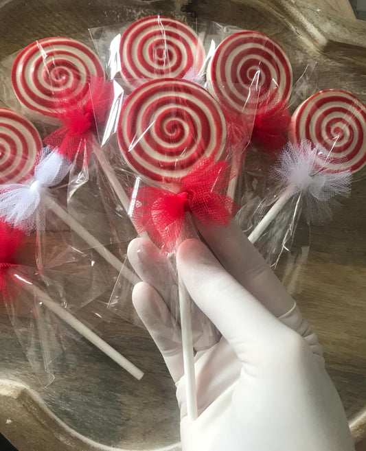 Red and white spiral lollipops on sticks with a hand wearing a white glove holding one, on a wooden surface.