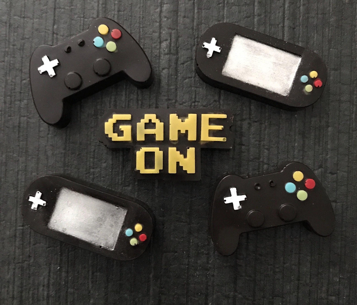Four black game controllers with colorful buttons on a dark textured background with 'GAME ON' text.