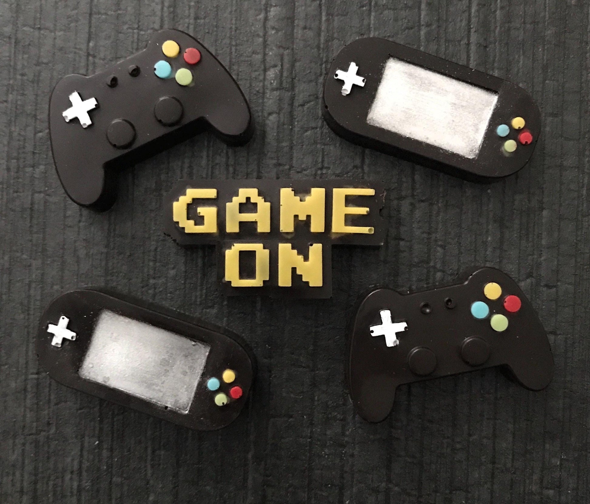 Four black game controllers with colorful buttons on a dark textured background with 'GAME ON' text.
